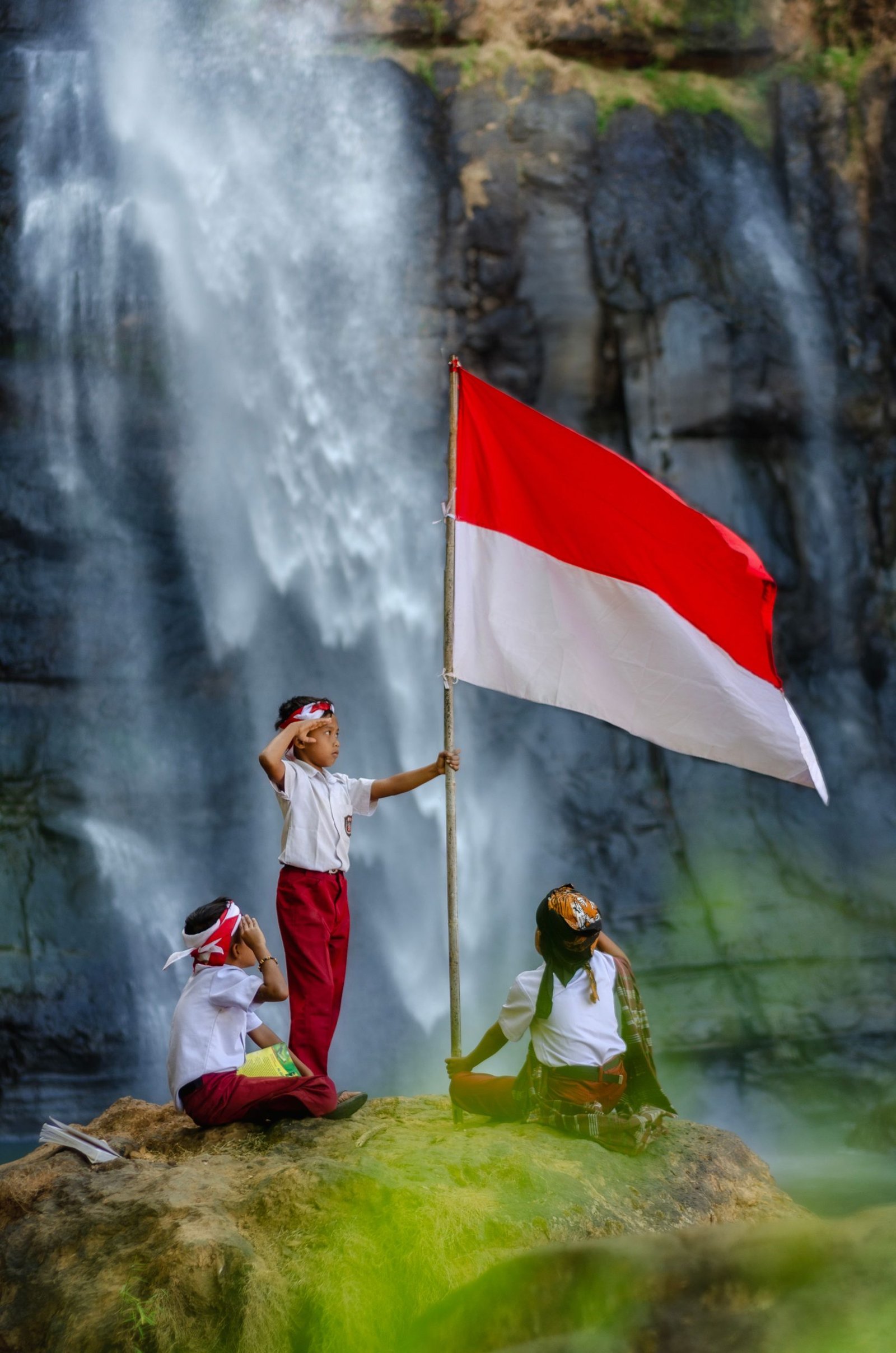 Children holding the Indonesian flag near a waterfall in rural Jawa Barat, Indonesia.