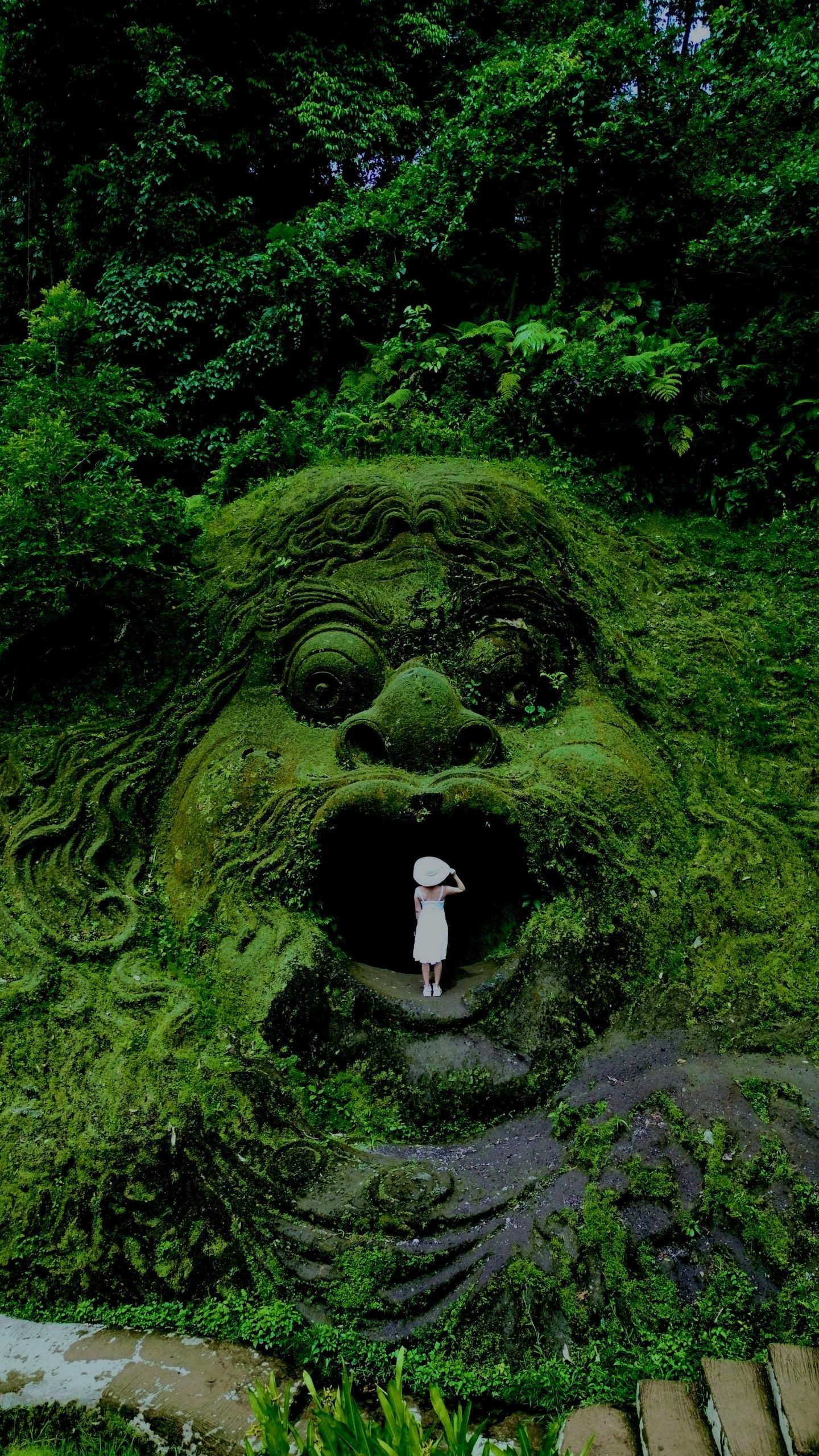A mysterious stone carving in Bali's jungle with a person exploring its entrance, surrounded by lush greenery.